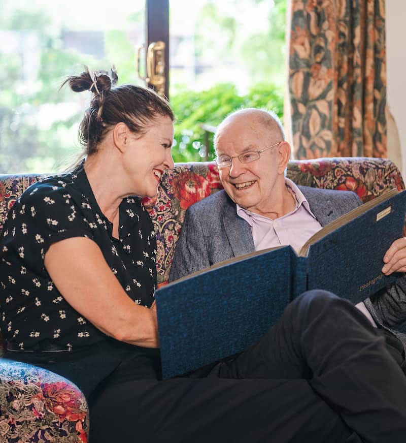 A live-in carer and an older man looking through a photograph album in his front room